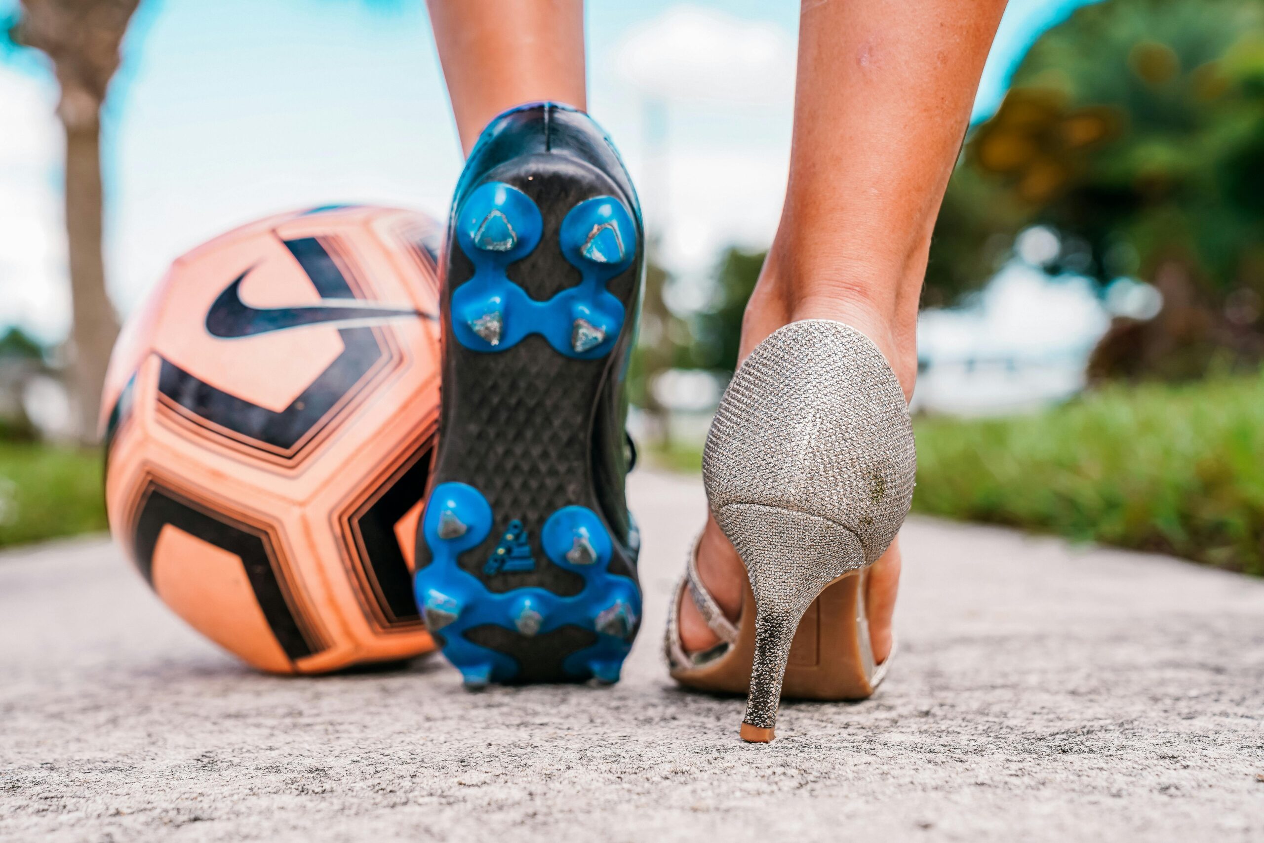 Juxtaposition of a soccer cleat and high heel on a sunny path, symbolizing diversity.